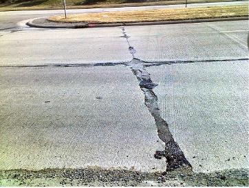 This picture shows a closer view of a severely distressed concrete pavement with severe spalling along the longitudinal and transverse joints. The joints seem to have been filled with joint sealer.